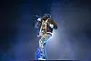 Meek Mill raps onstage in blue lighting during a concert at State Farm Arena.