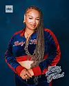 Woman posing in a navy and red jacket with braided hair against a blue background.