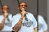 Performer in sunglasses sings into a microphone while wearing a graphic T-shirt.