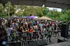 Large outdoor-event crowd standing behind barricades beneath a covered stage area.