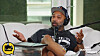 Man speaking into a microphone on a couch during a podcast recording.