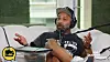 Man speaking into a microphone on a couch during a podcast recording.