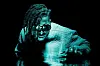 Flying Lotus in water up to his chest with dreads and glasses.