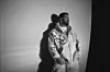 Drake leans againsta wall in black and white wearing a chain and a letterman's jacket.