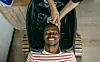 A smiling Black man has his hair washed at the barber.