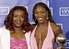 Serena and her sister posing for a photo wearing pink and holding a trophy.