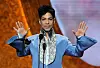 Prince in a blue suit holding his hands up in front of him.