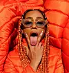 Boston rapper, BIA, in orange braids and puffy jacket making the v sign with tongue out