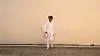 Santigold in an all white jumpsuit leaning against a blank, tan wall and holding a tamboreen.
