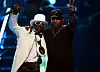 Flavor Flav, wearing all white and hat, Chuck D, wearing black shirt and hat.