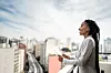 A black womaln holding an ipad looks out over the city smiling.