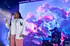Yaya Bey wearing a new york baseball jersy performing on stage in front a psychadelic screen with pink and blue clouds.