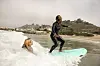 A Black woman on a surfboard with antoher black woman pushing the board behind her.