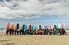 A large group of women posing for a photo on the beach with their brightly colored surfboards popping up in the background.