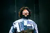 Bas wearing a patchwork Jean jacket and round sunglasses.