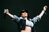 Keyshia Cole throws her hands up during her performance, wearing a sports braw covered by a longsleeved crop top jacket with the sleaves rolled up.